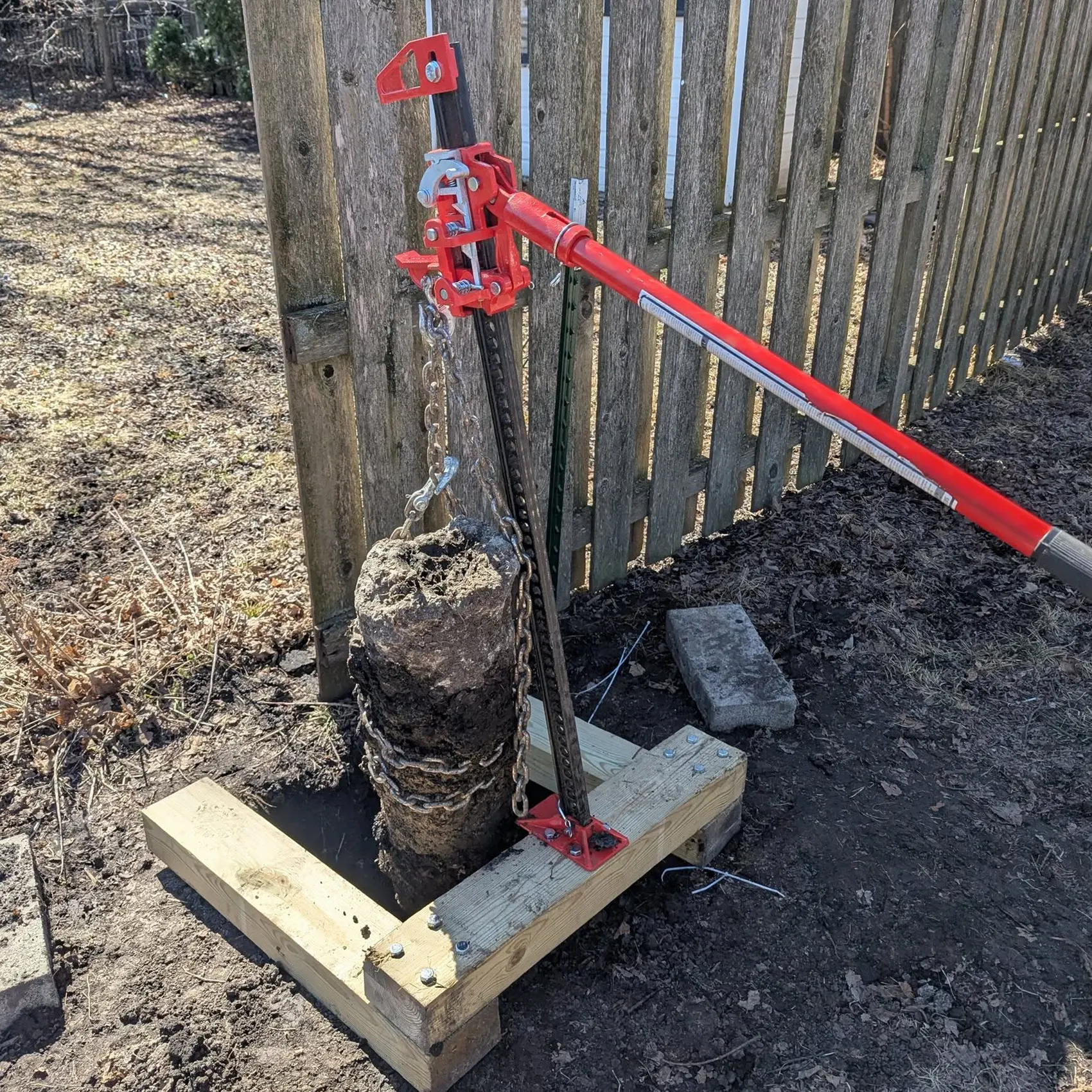 A utility jack being used to pull an old concrete fence footing out of the ground